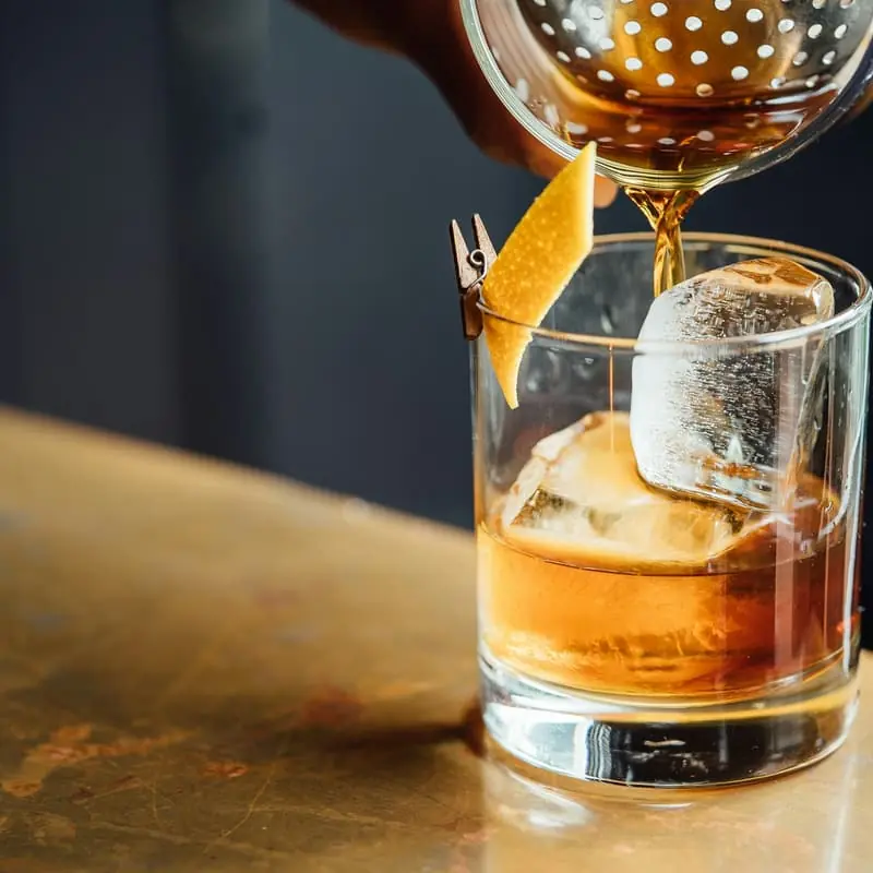 Cóctel colándose sobre un vaso con hielo en la barra de un bar