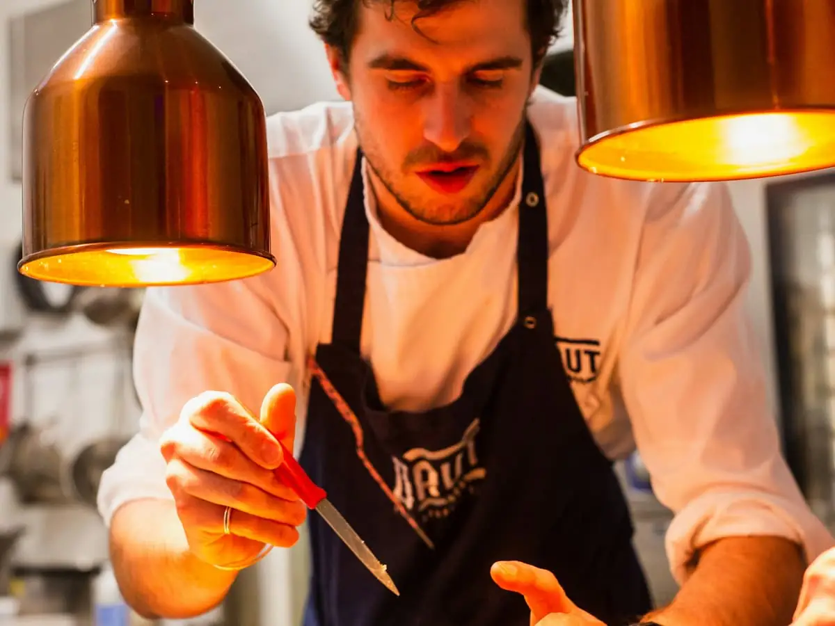 Cocinero terminando un plato bajo las lámparas de calor de una cocina profesional